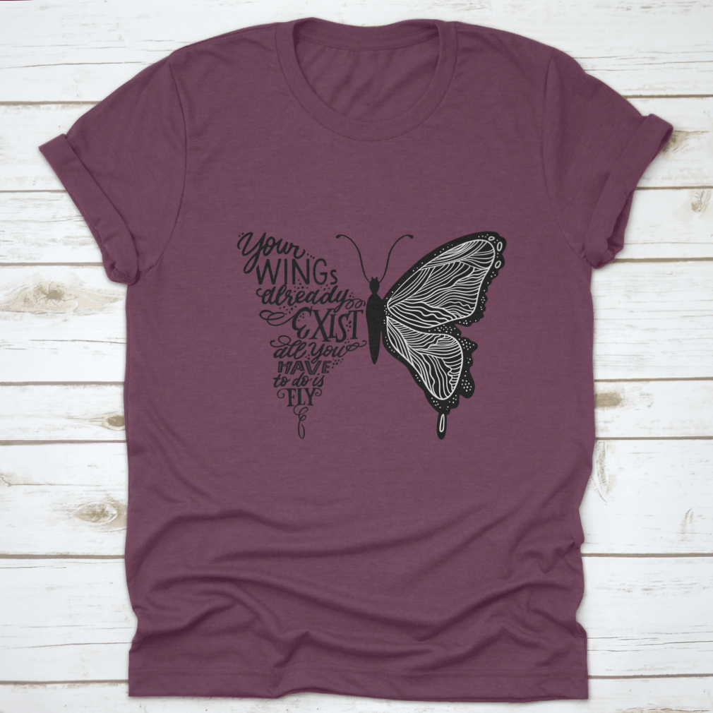 A stylish t-shirt featuring hand lettering in a butterfly silhouette design, showcasing the phrase 'Your Wings Already Exists All' on a soft fabric.