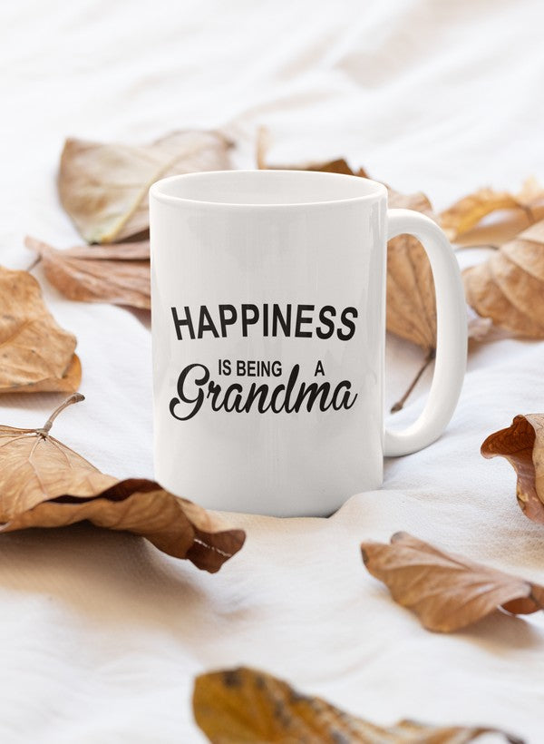 A glossy white ceramic mug with the phrase 'Happiness Is Being A Grandma' printed in colorful letters, featuring a sturdy handle.