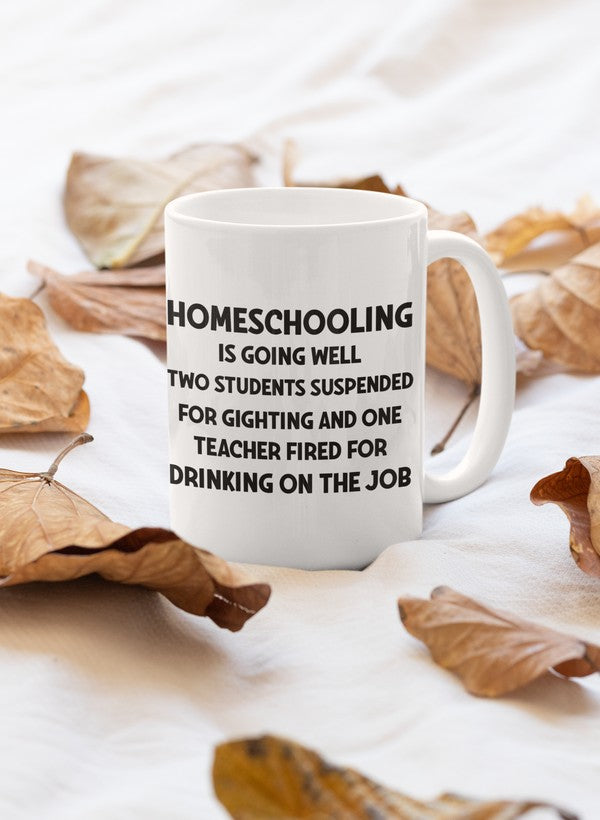 A glossy white ceramic mug with the phrase 'Homeschooling Is Going Well' printed in colorful letters, featuring a sturdy handle.