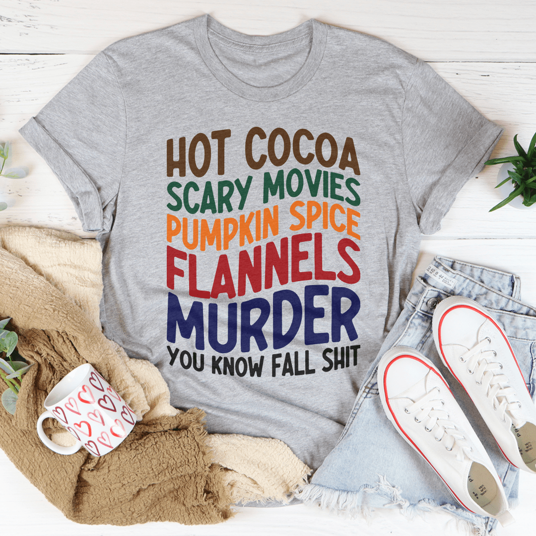 A cozy Hot Cocoa Scary Movies Pumpkin Spice Flannels T-Shirt displayed on a wooden background, showcasing its soft fabric and vibrant autumn-themed design.