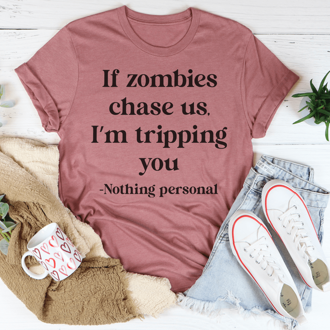 A humorous t-shirt featuring the phrase 'If Zombies Chase Us I'm Tripping You' printed on soft cotton fabric, perfect for zombie lovers.