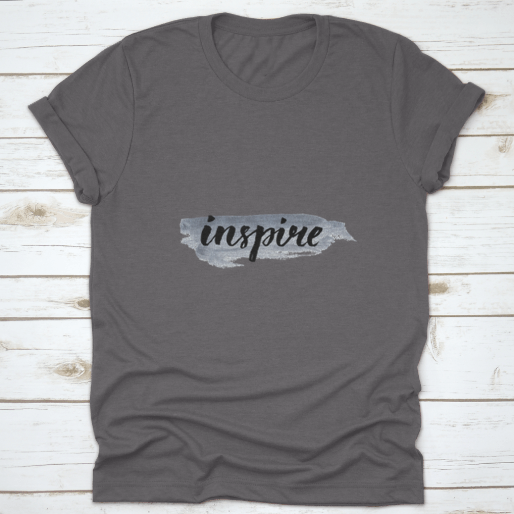 Inspire Calligraphy Word Handwritten on Silver Paint, showcasing elegant lettering on a stylish fabric background.