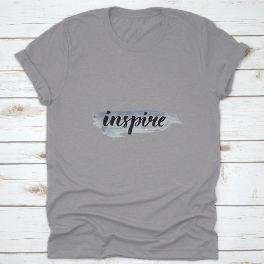 Inspire Calligraphy Word Handwritten on Silver Paint, showcasing elegant lettering on a stylish fabric background.