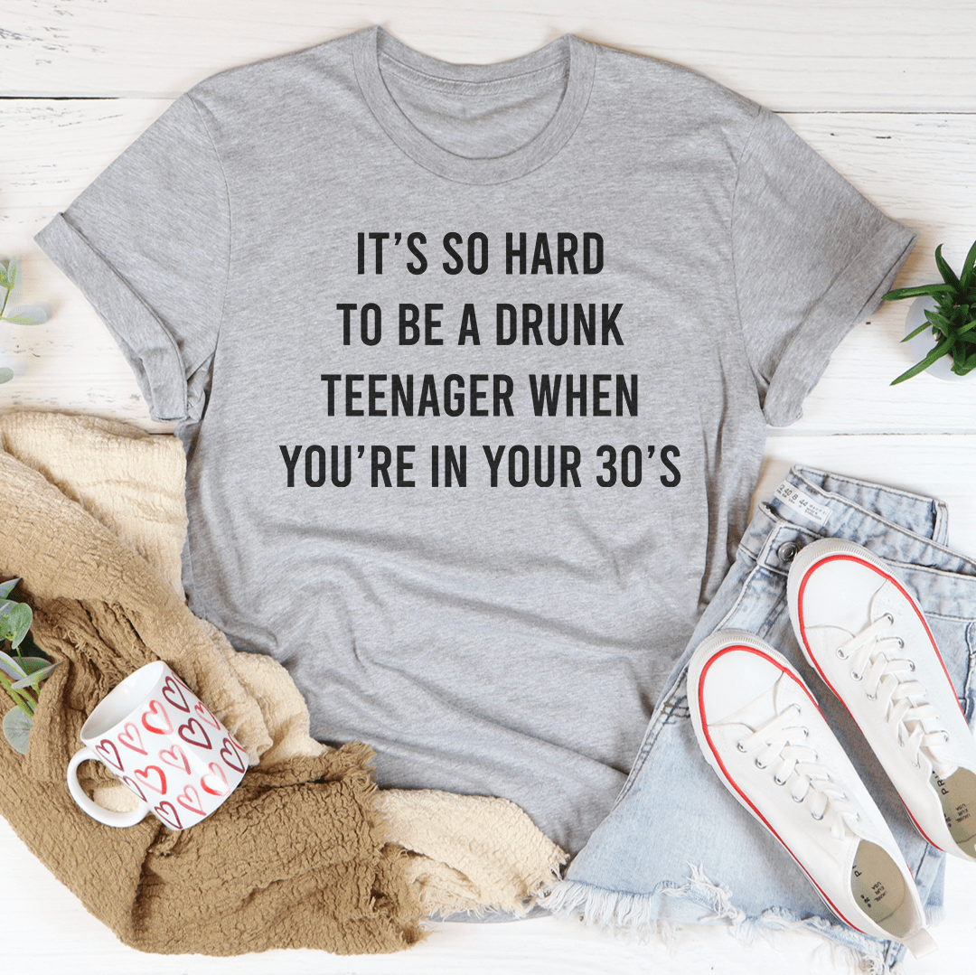 A humorous T-shirt reading 'It's So Hard To Be A Drunk T-Shirtnager When You're In Yours 30's', made from soft cotton with double stitching.