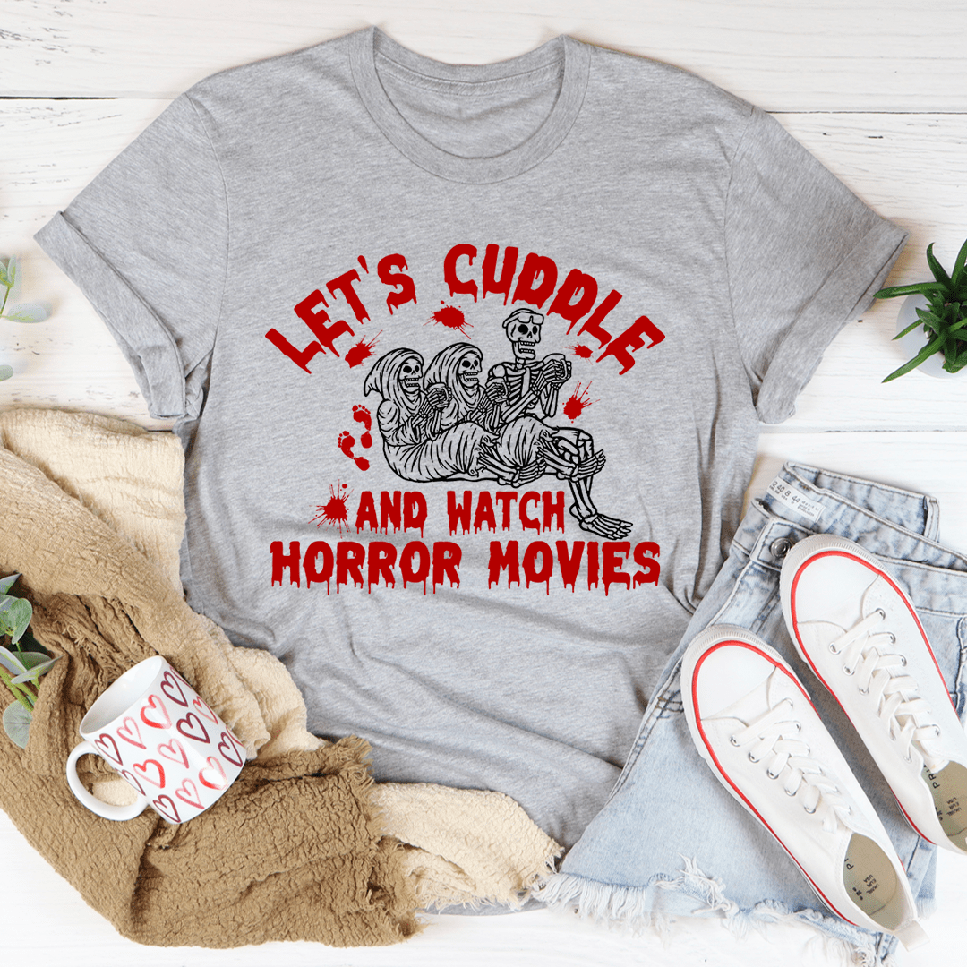 A cozy black t-shirt featuring the phrase 'Let's Cuddle And Watch Horror Movies' in bold white letters, perfect for movie nights.