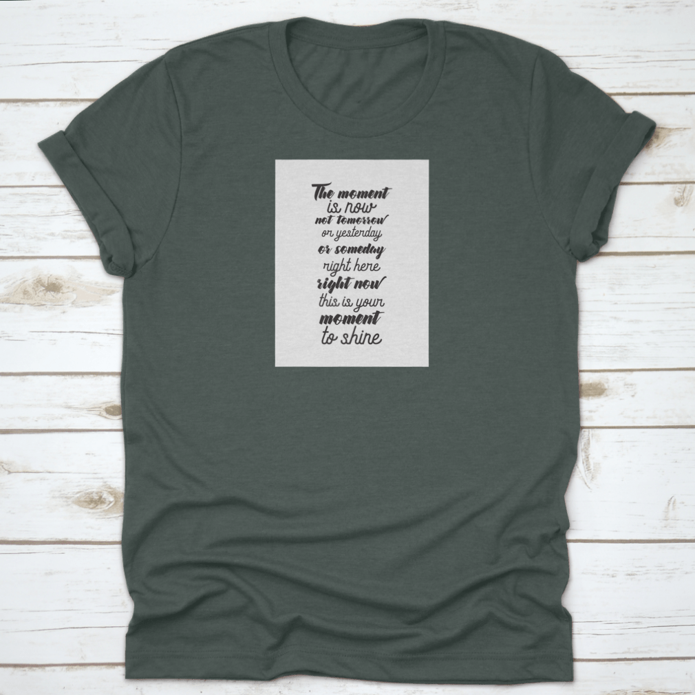 A motivational T-shirt featuring the quote 'The Moment Is Now, Not Tomorrow', made from soft cotton fabric, displayed on a neutral background.