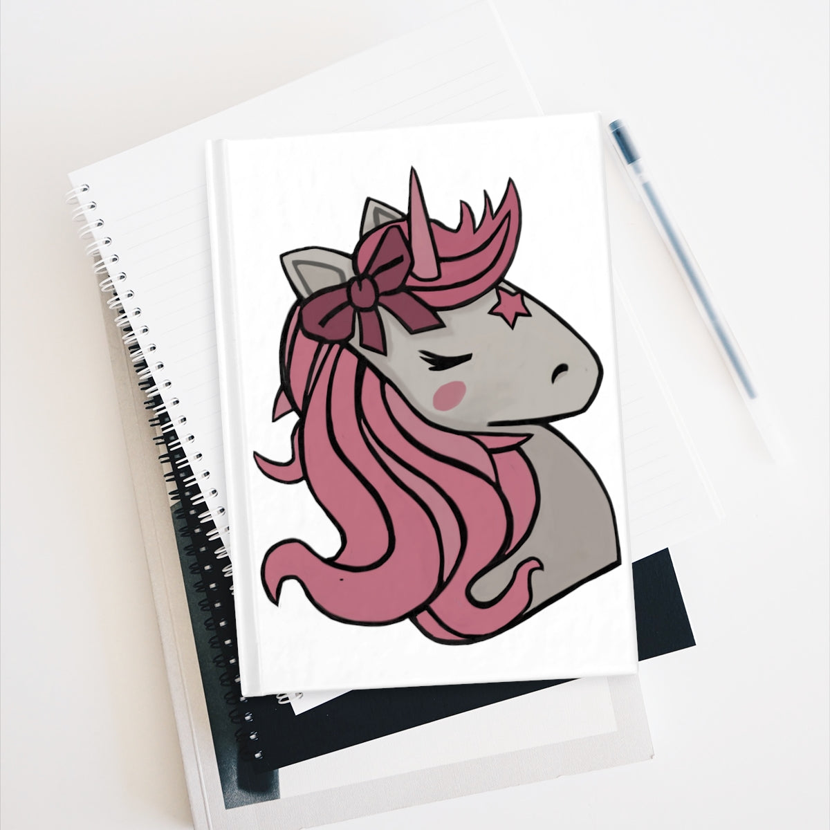 A hardcover journal featuring a whimsical pink hair unicorn design, showcasing a durable wraparound print and ruled line pages.