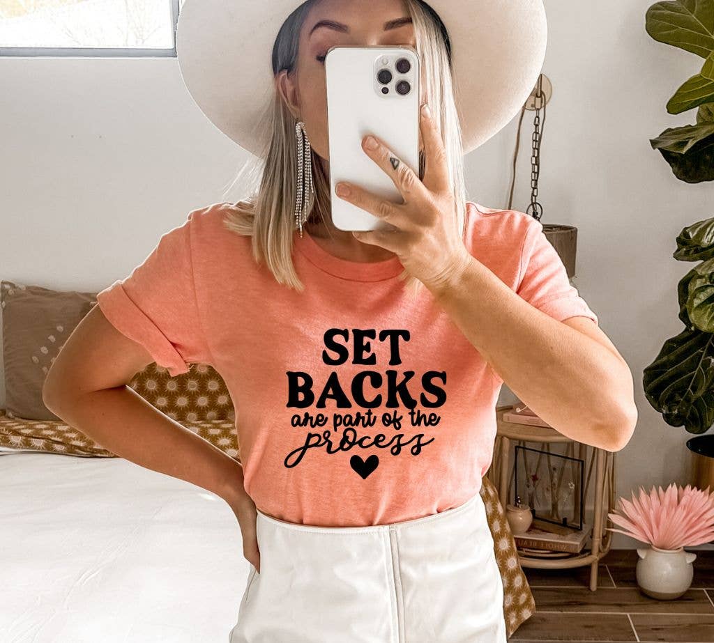 A stylish black T-shirt featuring the motivational phrase 'Set Backs Are Part Of The Process' printed in a modern font, made from soft ring spun cotton.
