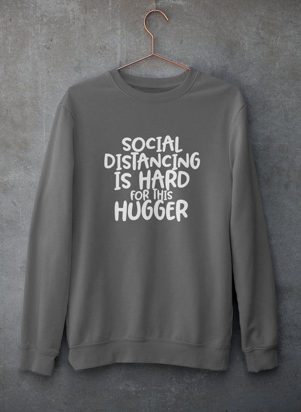 A cozy sweatshirt featuring the phrase 'Social Distancing Is Hard For This Hugger', made from a soft cotton/poly fleece blend.