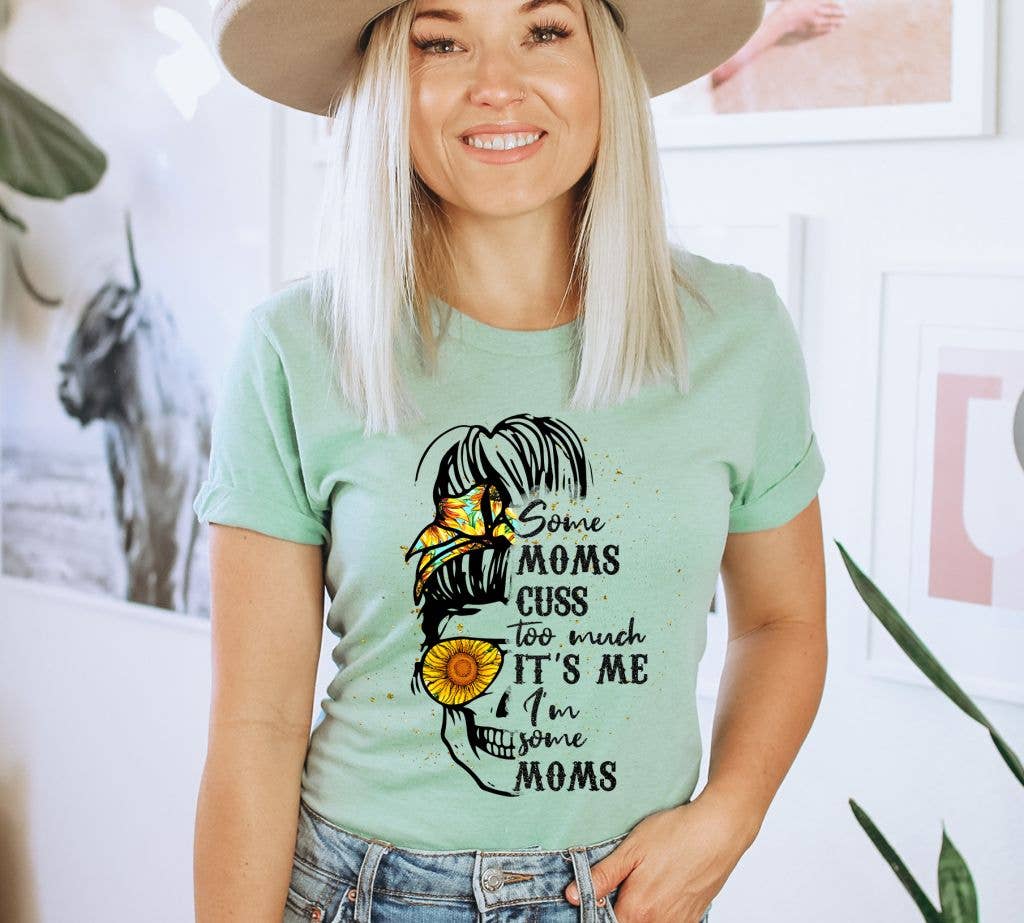 A stylish black T-shirt featuring the humorous text 'Some Moms Cuss Too Much It's Me I Am', made from soft ring spun cotton.