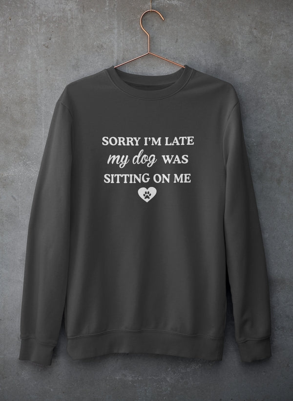 A cozy sweatshirt featuring the phrase 'Sorry I'm Late My Dog Was Sitting On Me' in a playful font, perfect for dog lovers.