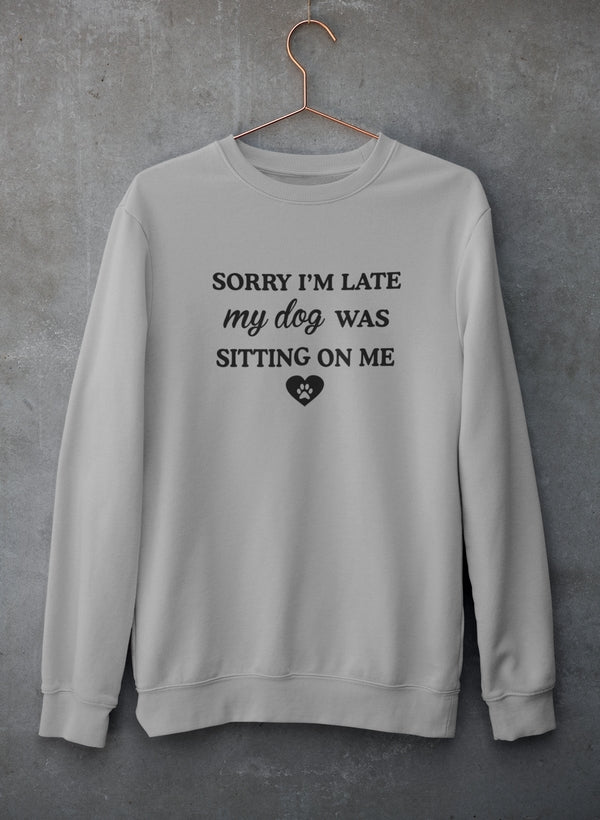 A cozy sweatshirt featuring the phrase 'Sorry I'm Late My Dog Was Sitting On Me' in a playful font, perfect for dog lovers.