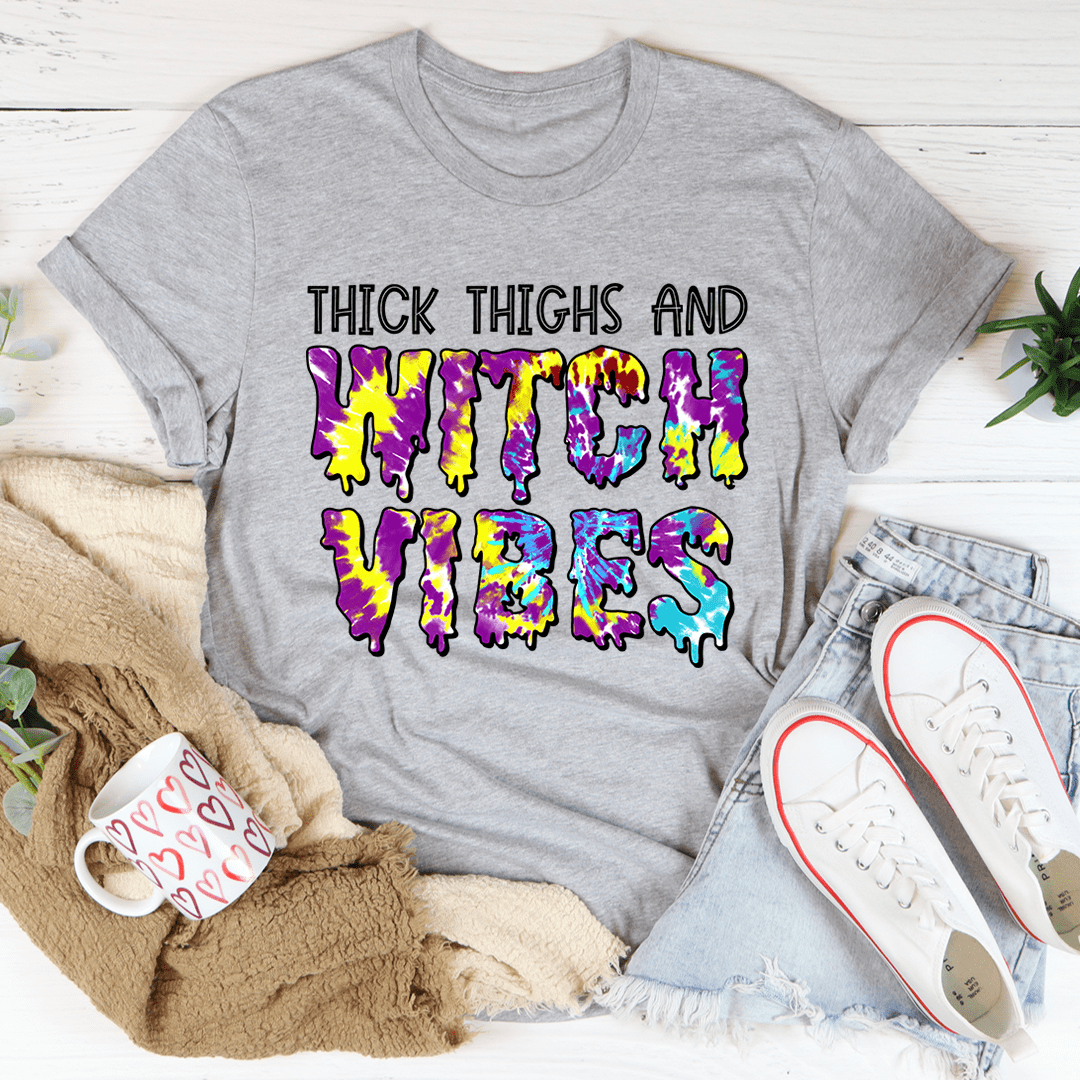 A stylish Halloween tee featuring the phrase 'Thick Thighs And Witch Vibes' printed in vibrant colors on soft cotton fabric.