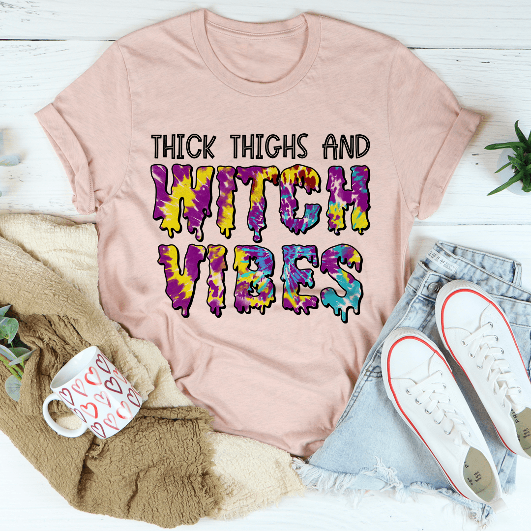 A stylish Halloween tee featuring the phrase 'Thick Thighs And Witch Vibes' printed in vibrant colors on soft cotton fabric.