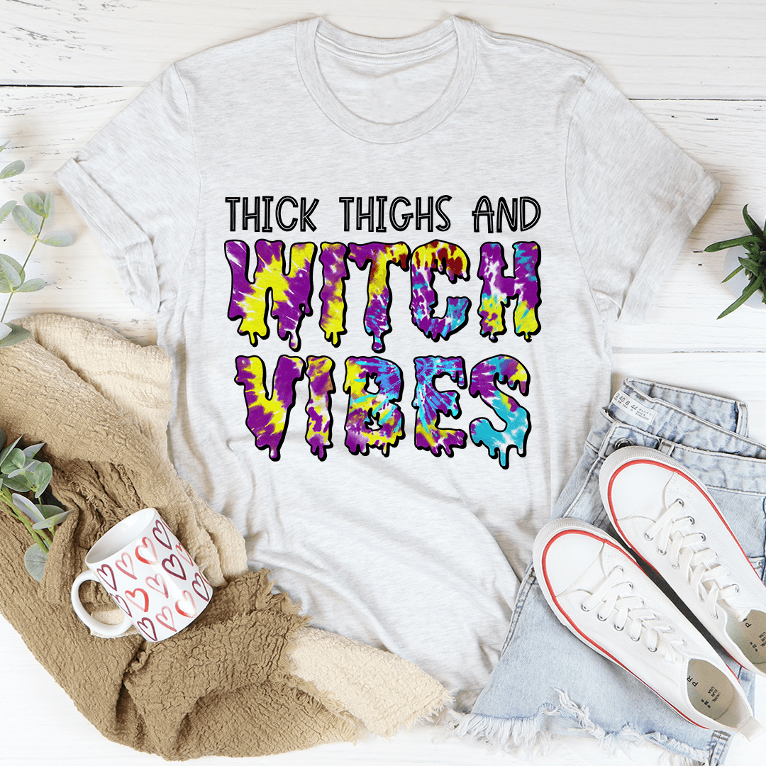 A stylish Halloween tee featuring the phrase 'Thick Thighs And Witch Vibes' printed in vibrant colors on soft cotton fabric.