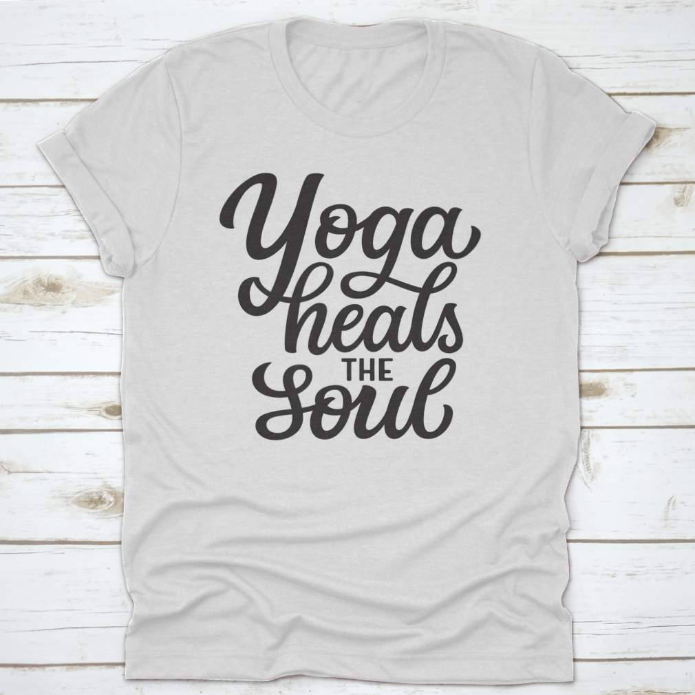 A hand-drawn quote 'Yoga Heals The Soul' printed on a white cotton t-shirt, showcasing a stylish and inspirational design.