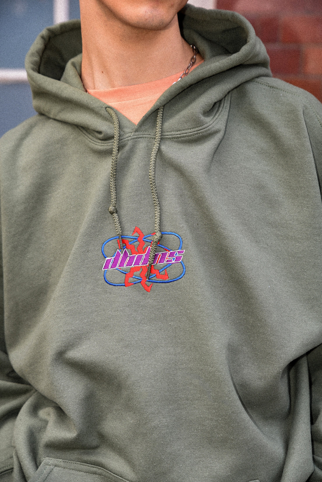 Military green unisex hoodie with futuristic logo embroidery, showcasing a relaxed fit and heavyweight cotton material.