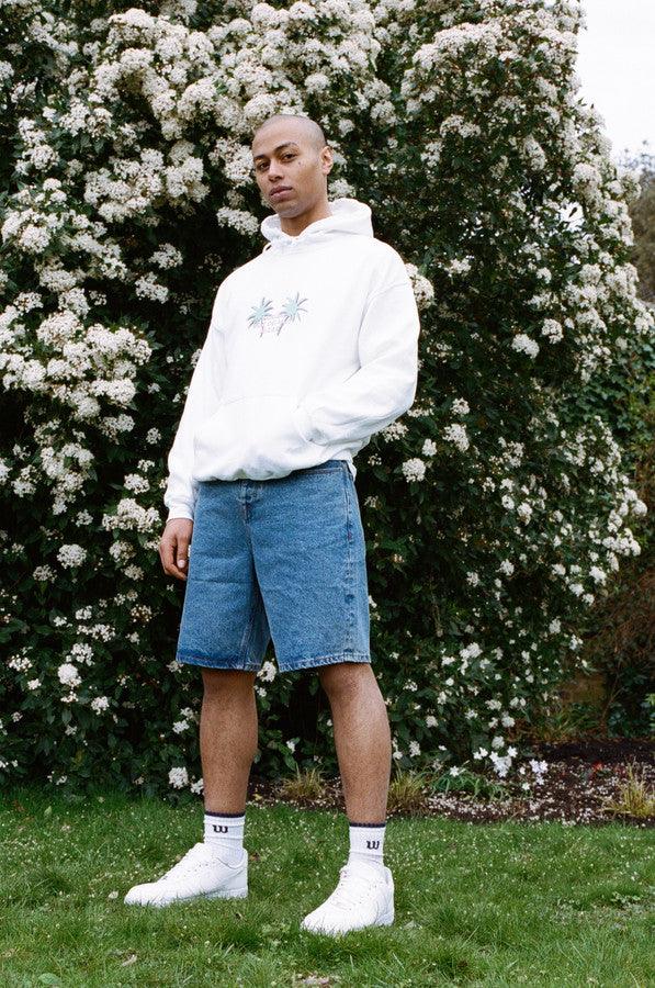 White hoodie featuring a vibrant tropical palm tree print on front and back, showcasing a relaxed fit and woven label details.