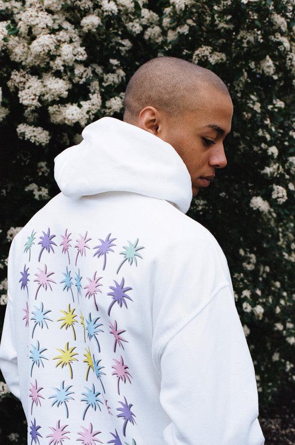 White hoodie featuring a vibrant tropical palm tree print on front and back, showcasing a relaxed fit and woven label details.
