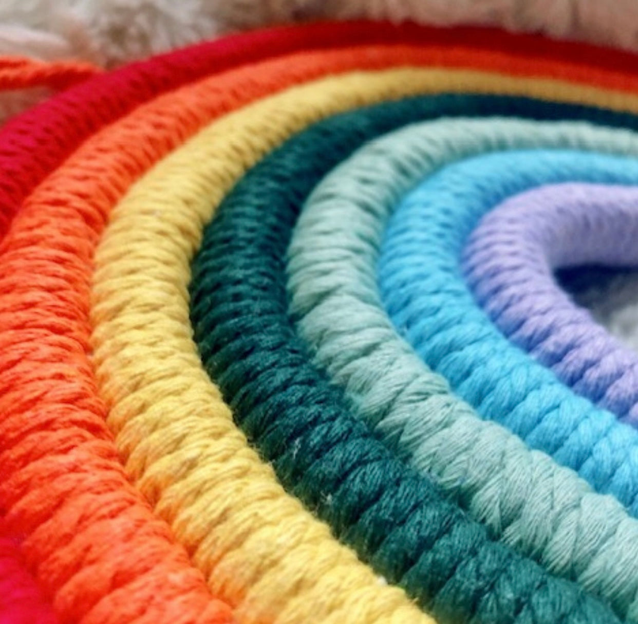 A colorful handmade rope rainbow wall hanging, featuring vibrant hues and a chunky design, perfect for nursery decor.