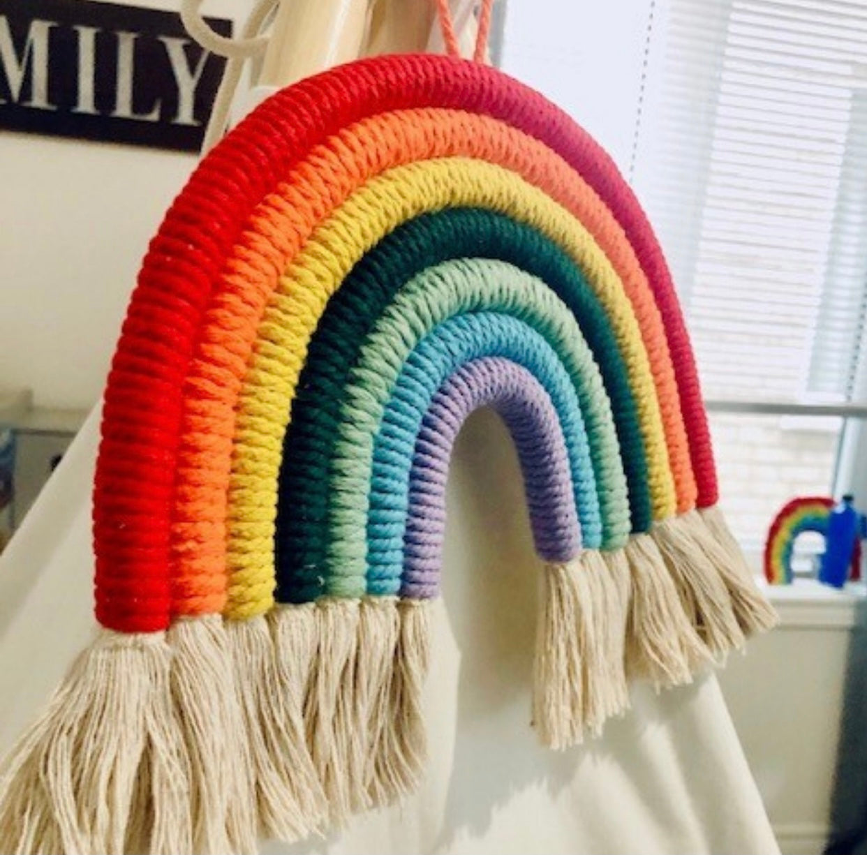 A colorful handmade rope rainbow wall hanging, featuring vibrant hues and a chunky design, perfect for nursery decor.