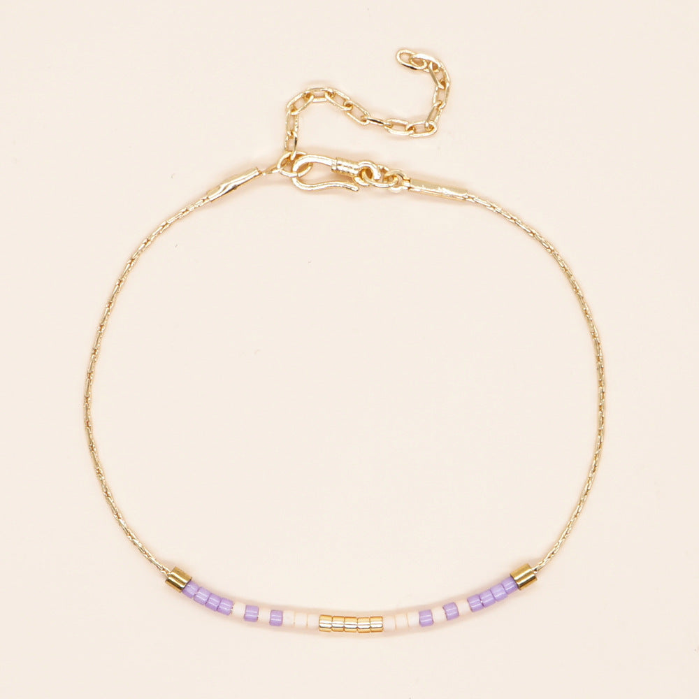 Delicate gold double-strand bracelet with colorful beaded accents, featuring a lobster claw closure.