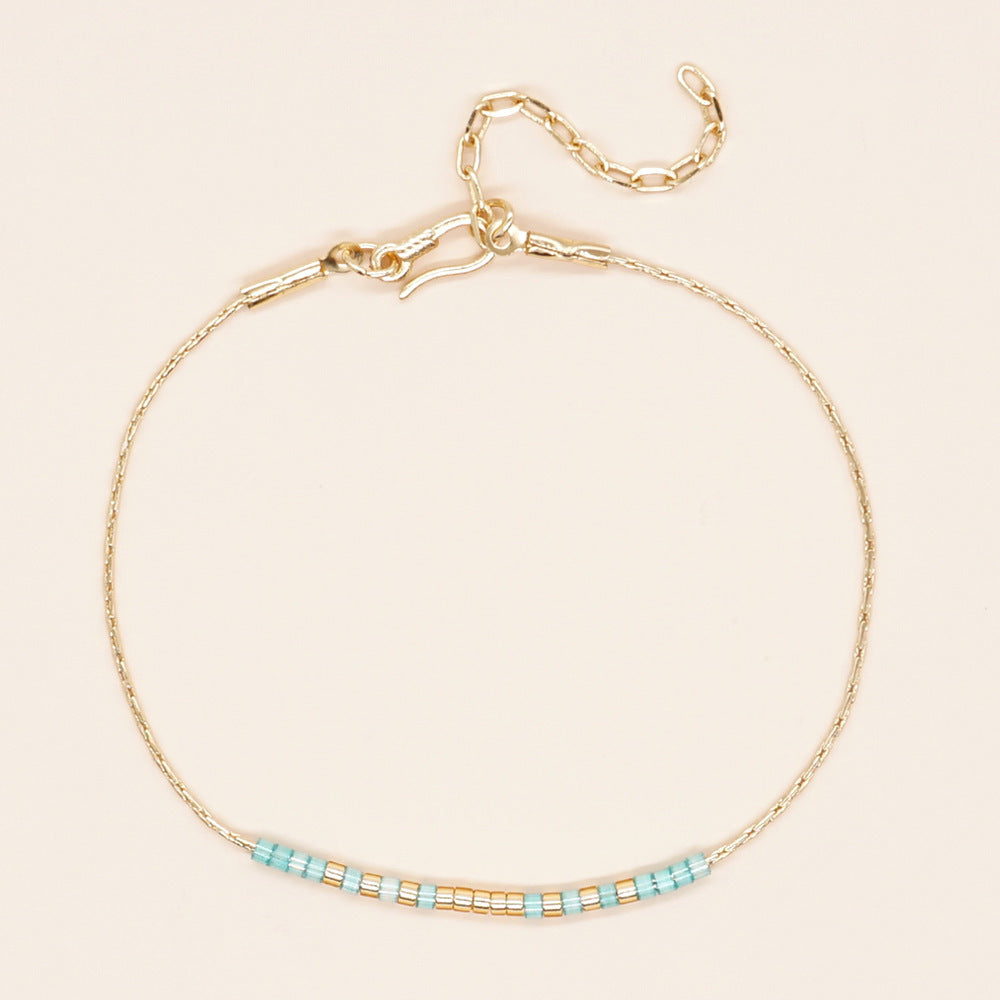 Delicate gold double-strand bracelet with colorful beads, featuring a lobster claw closure.