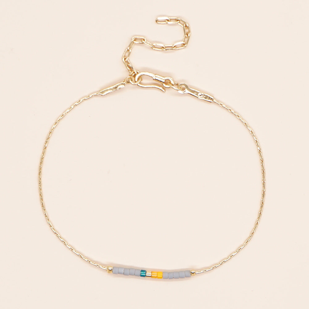 Delicate gold double-strand bracelet with colorful beads, featuring a lobster claw closure.
