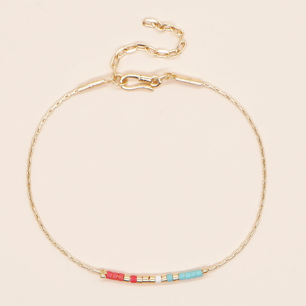 Delicate gold double-strand bracelet with colorful beads, featuring a lobster claw closure, showcasing minimalist design.