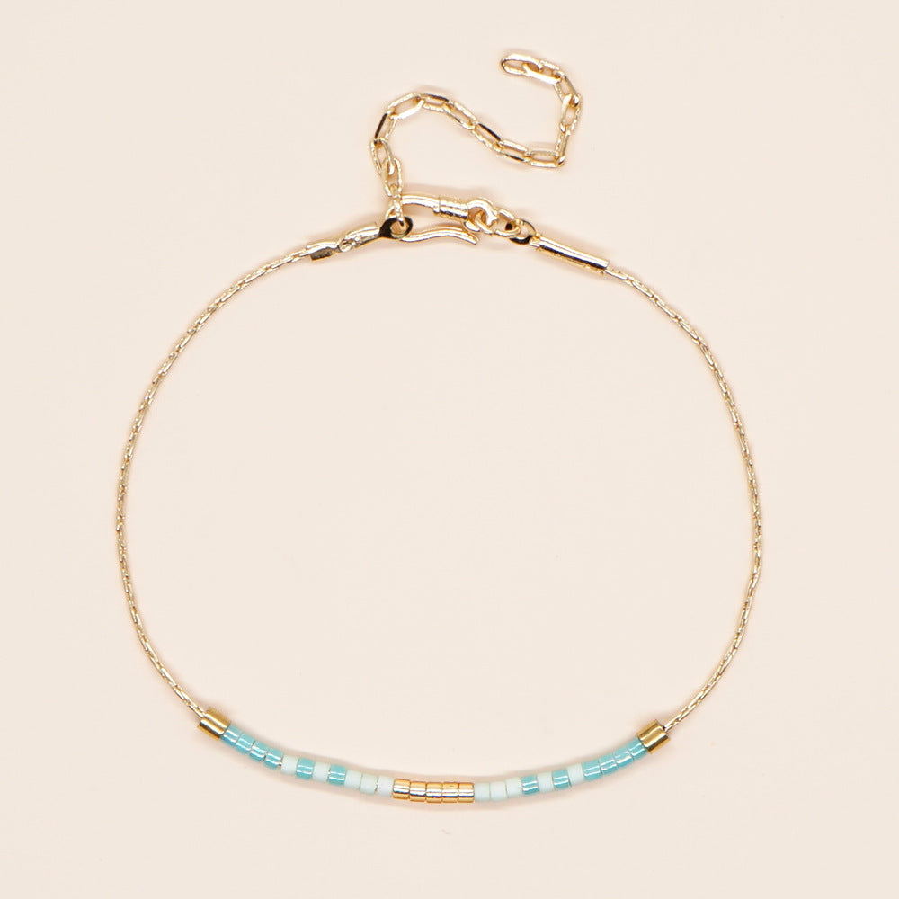 Delicate gold double-strand bracelet with colorful beads, featuring a lobster claw closure, showcasing minimalist style.