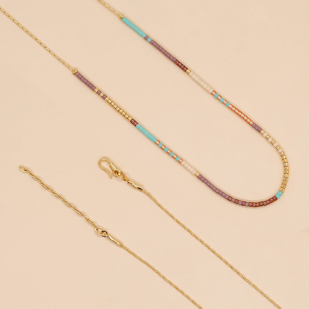 Delicate gold double-strand necklace with colorful beaded accents, featuring a lobster claw closure, elegantly displayed on a soft background.
