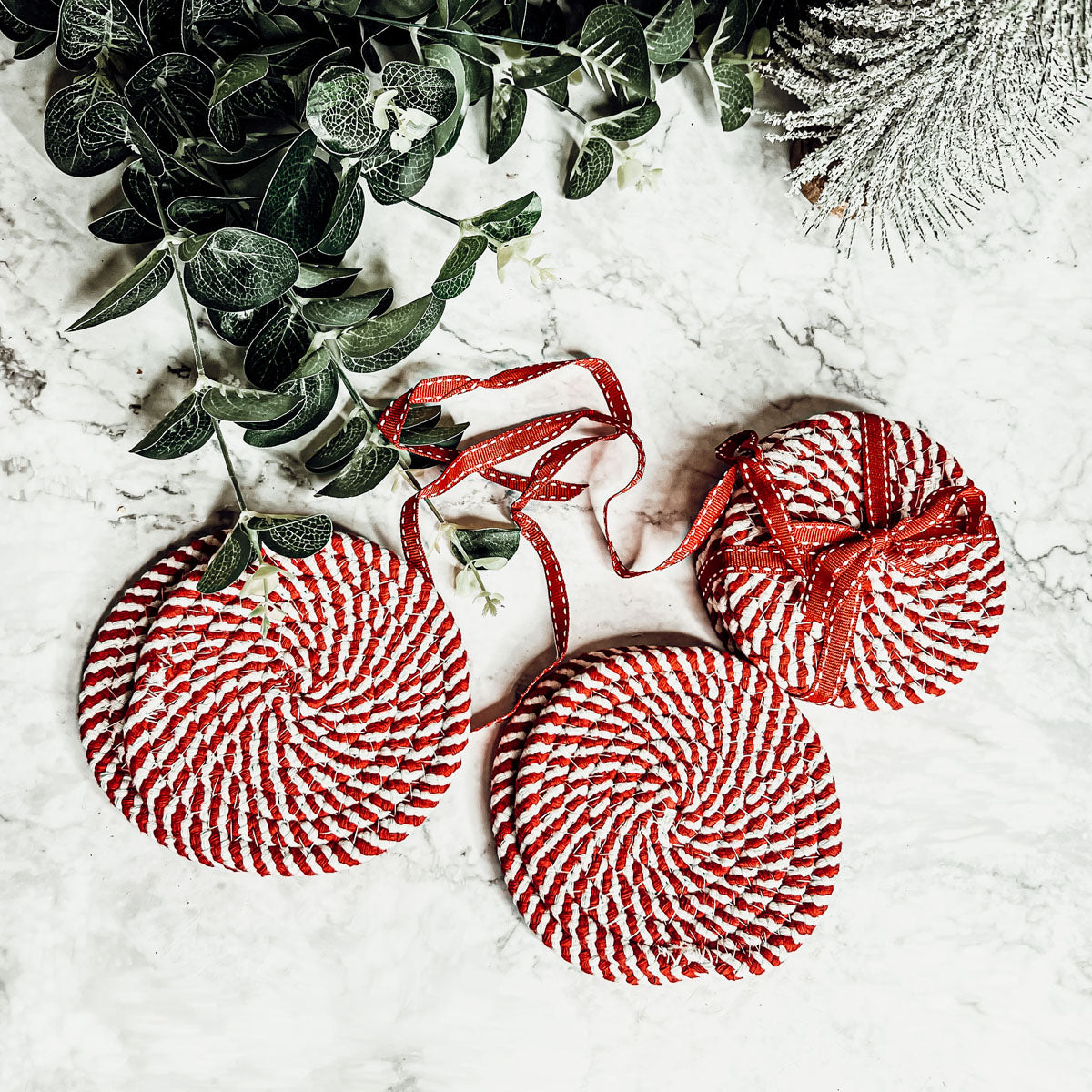 A set of four candy cane striped coasters with braided detail, perfect for holiday decor.