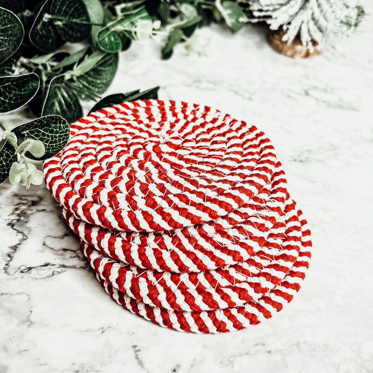A set of four candy cane striped coasters with braided detail, perfect for holiday decor.