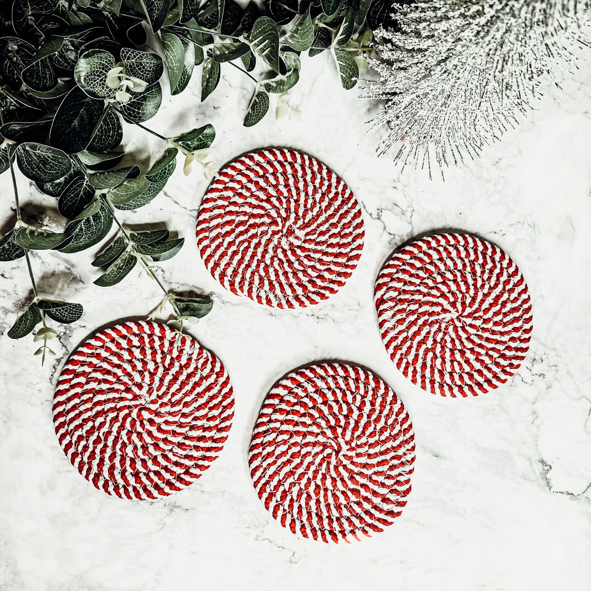 A set of four candy cane striped coasters with braided detail, perfect for holiday decor.