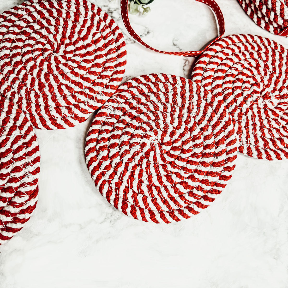 A set of four candy cane striped coasters with braided detail, perfect for holiday decor.