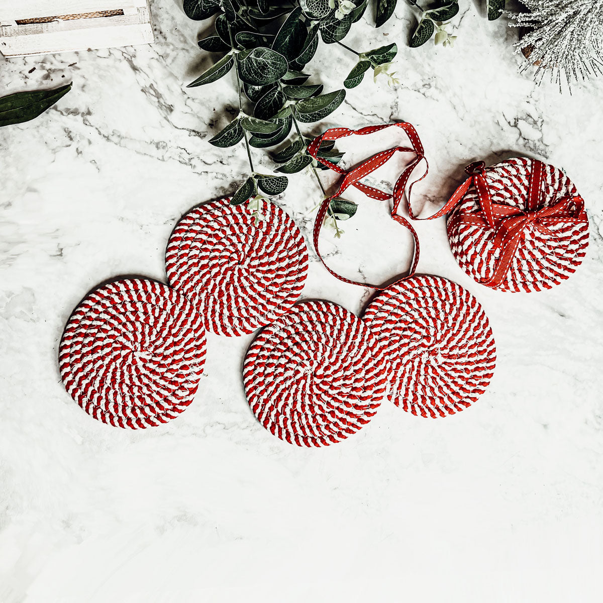 A set of four candy cane striped coasters with braided detail, perfect for holiday decor.