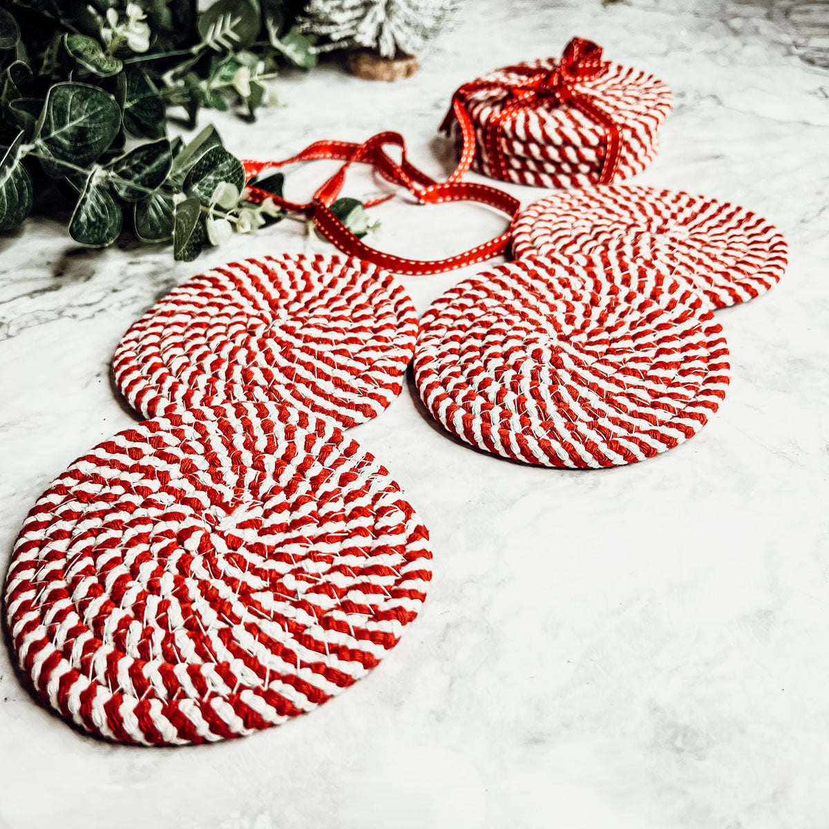 A set of four candy cane striped coasters with braided detail, perfect for holiday decor.