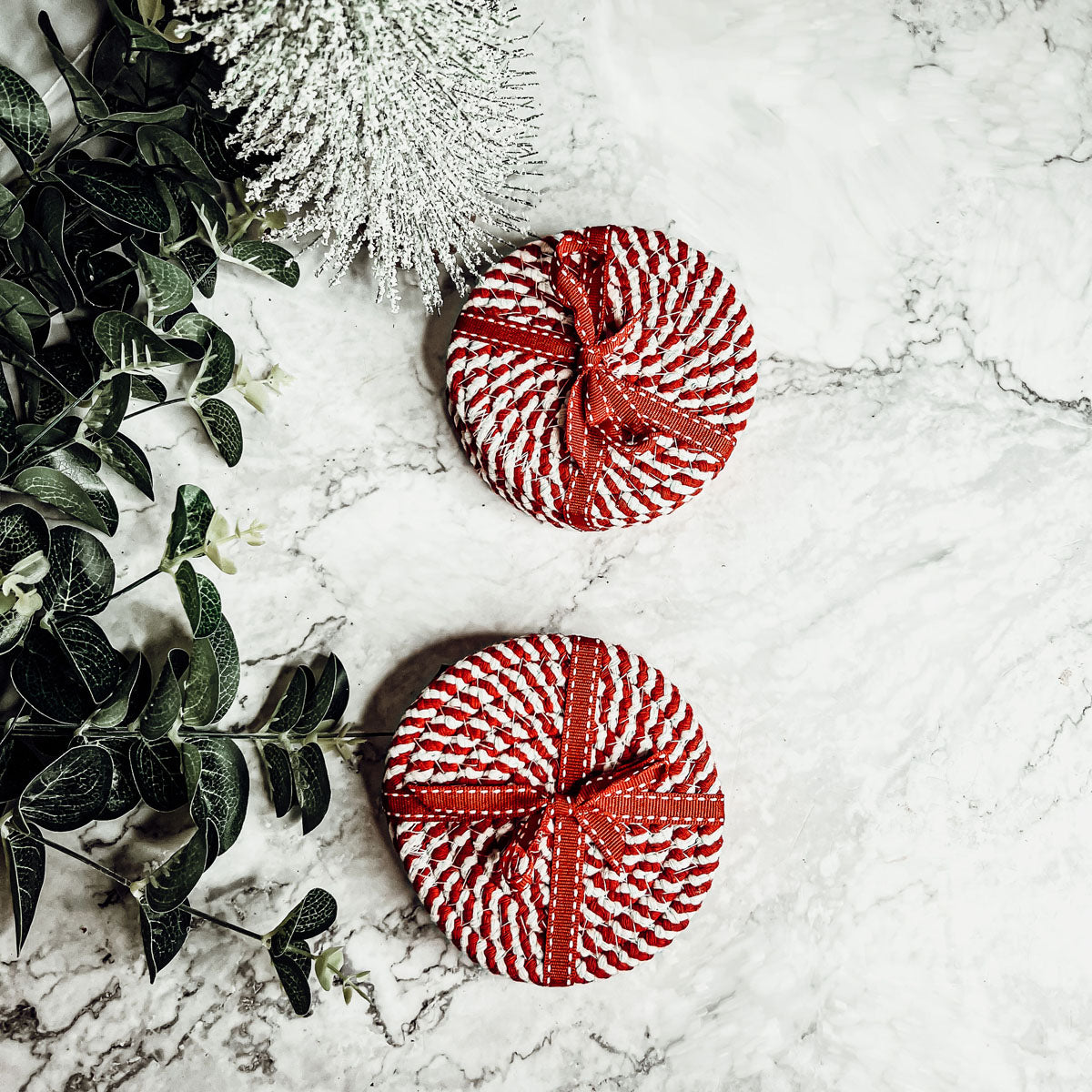 A set of four candy cane striped coasters with braided detail, perfect for holiday decor.