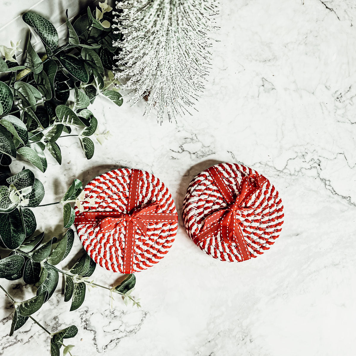A set of four candy cane striped coasters with braided detail, perfect for holiday decor.