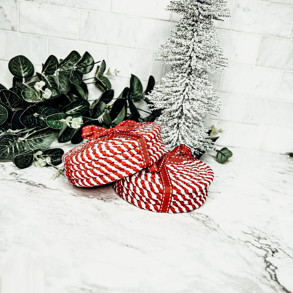 A set of four candy cane striped coasters with braided detail, perfect for holiday decor.