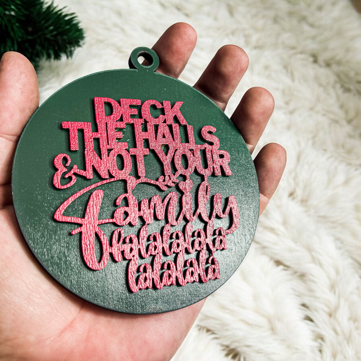 Colorful wooden ornament with the phrase 'Deck the Halls (and Not Your Family)', featuring a 3D design and rustic twine for hanging.