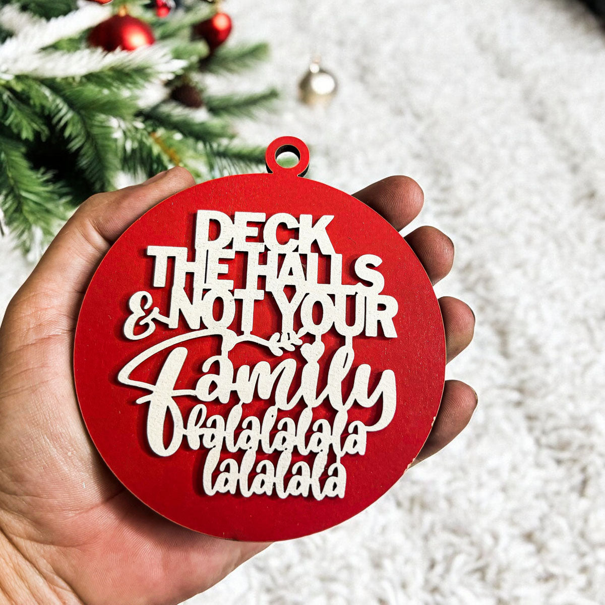 Colorful wooden ornament with the phrase 'Deck the Halls (and Not Your Family)', featuring a 3D design and rustic twine for hanging.