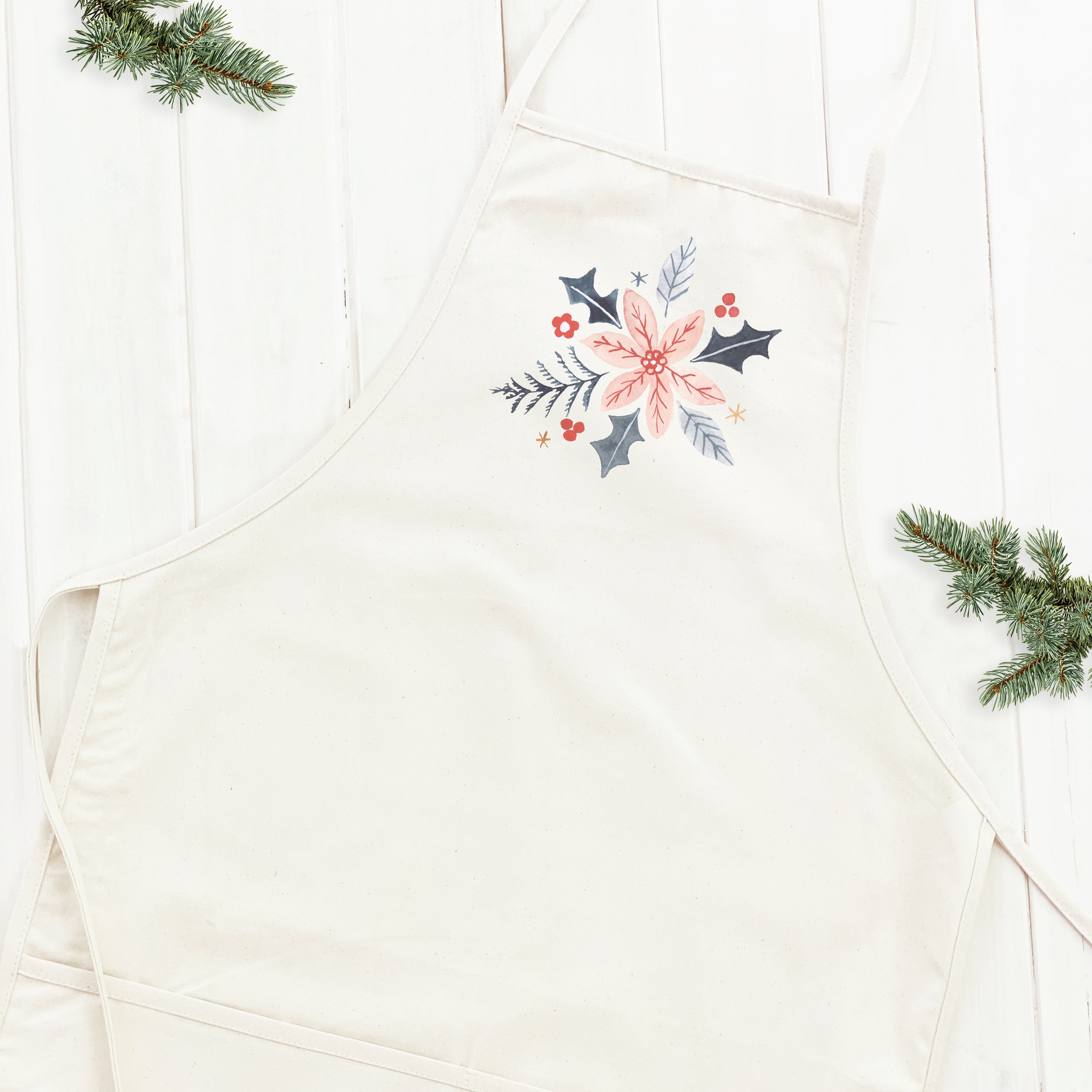 A stylish women's apron featuring a hand-drawn pink poinsettia design on durable cotton canvas fabric, with natural twill ties and a divided front pocket.