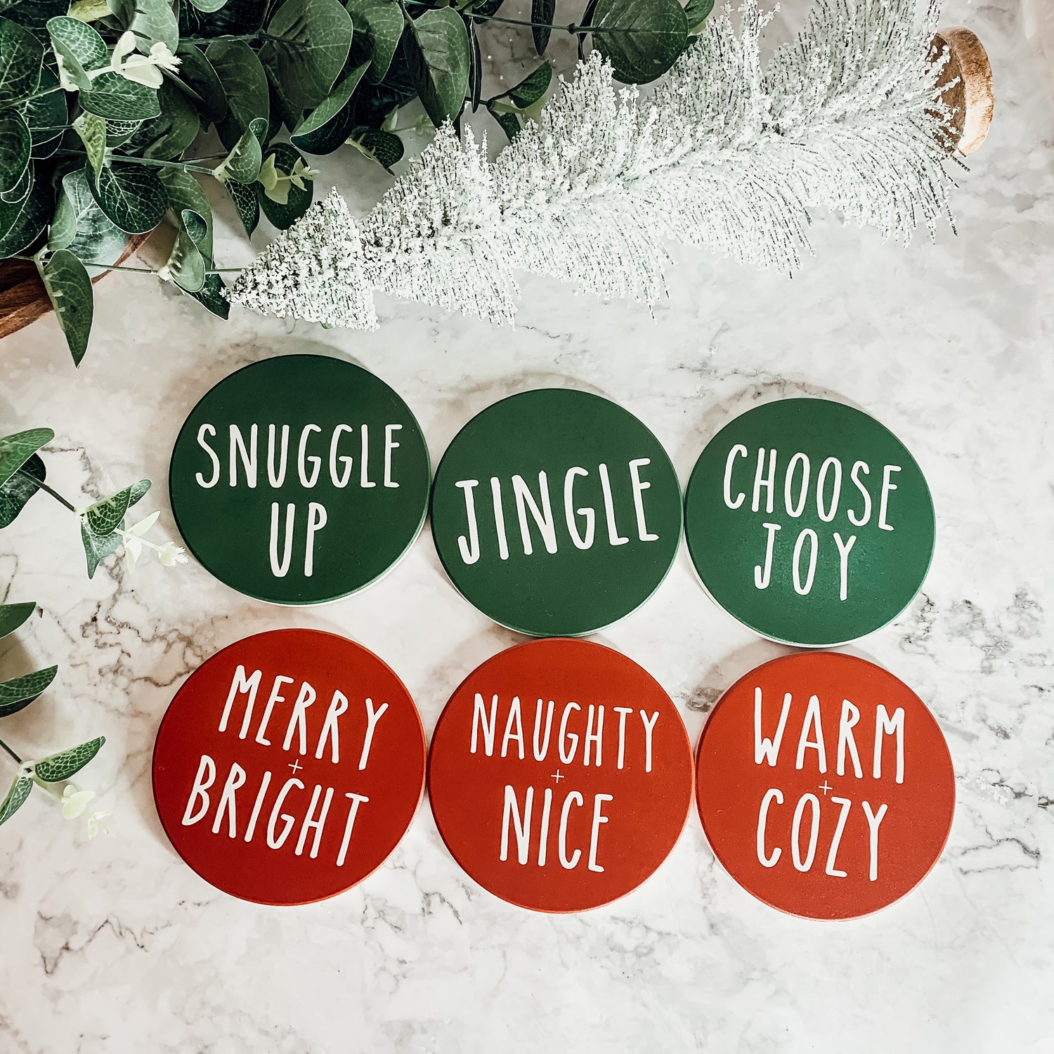 Set of six premium ceramic coasters with cork backing, featuring festive holiday designs including 'Choose Joy' and 'Merry + Bright'.