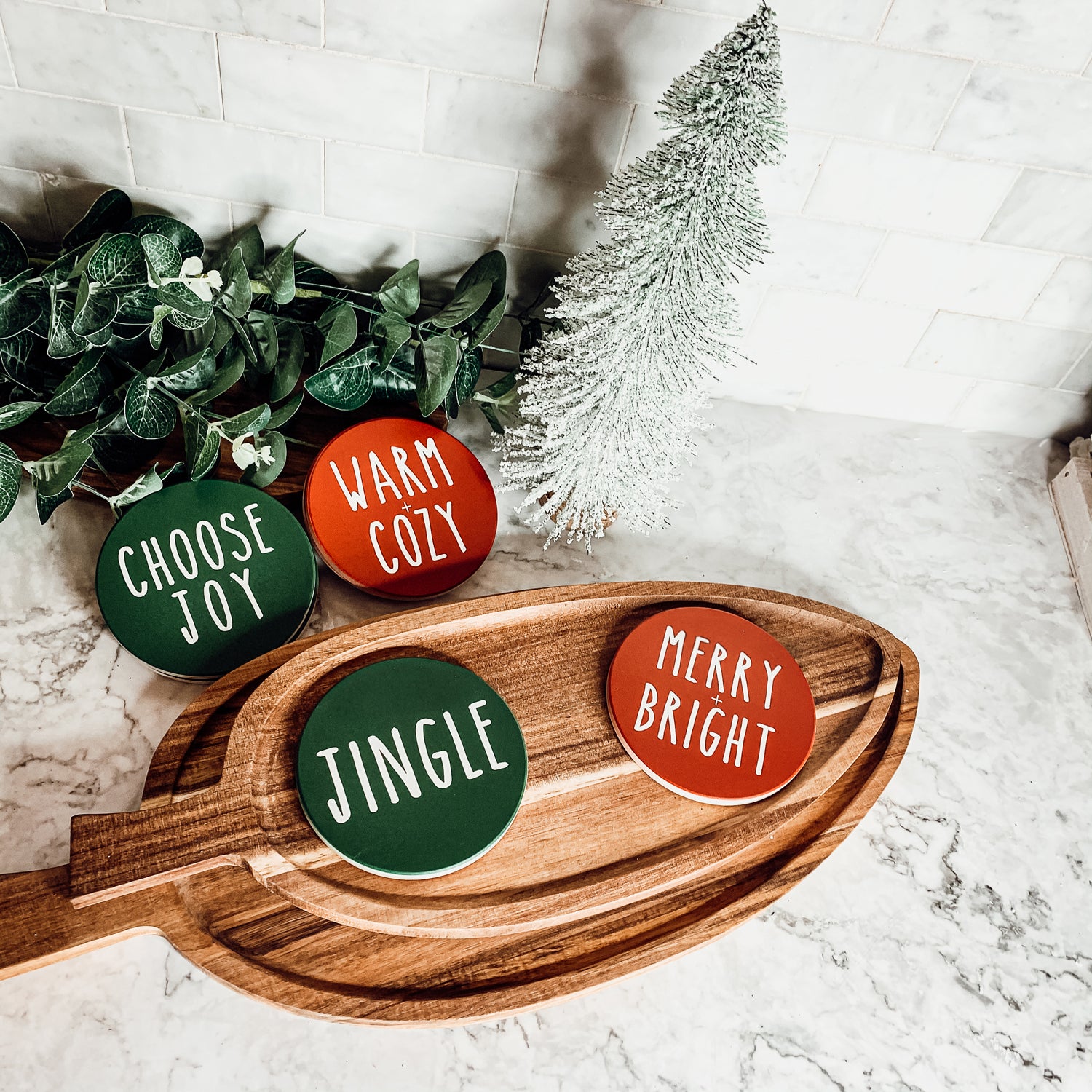 Set of six premium ceramic coasters with cork backing, featuring festive holiday designs including 'Choose Joy' and 'Merry + Bright'.