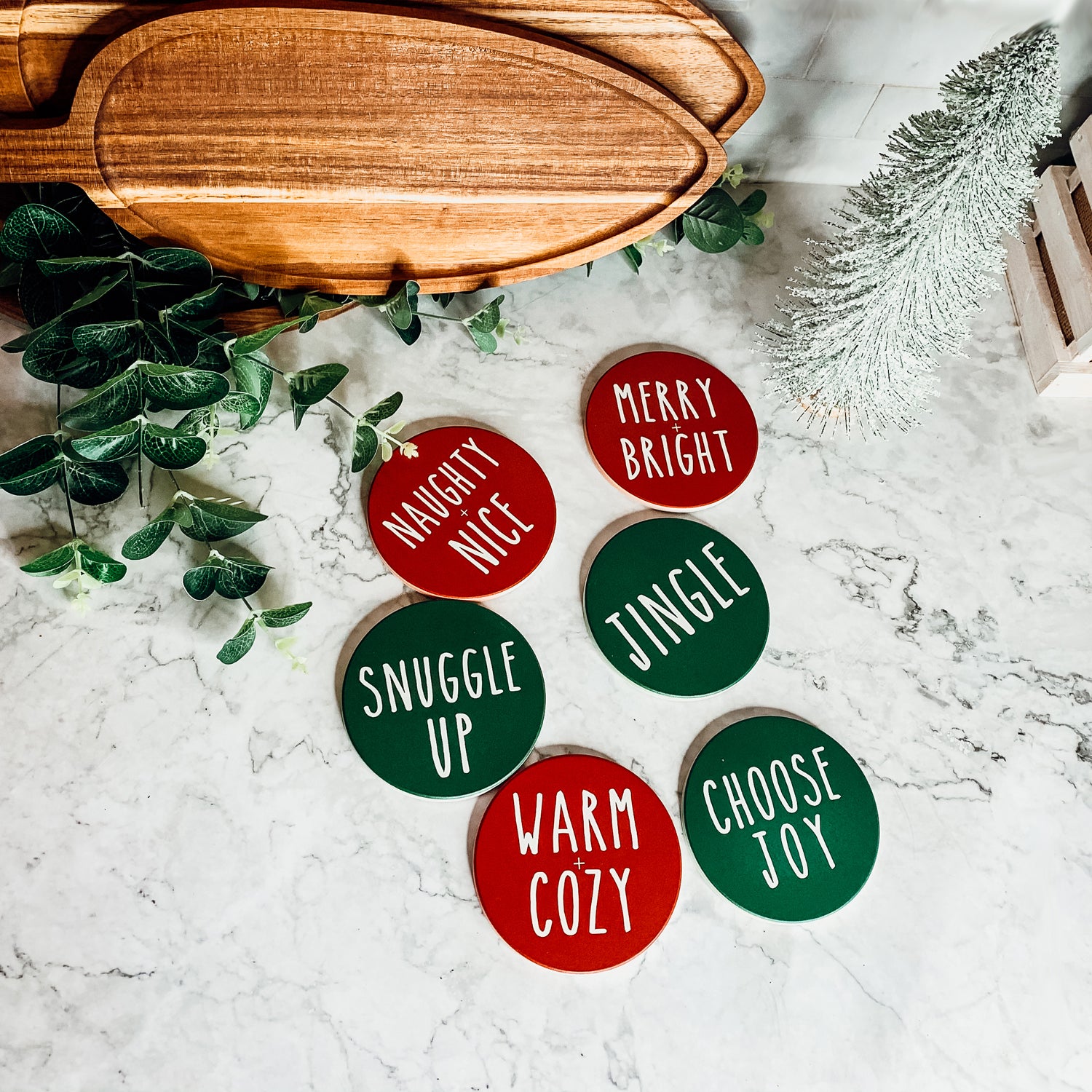 Set of six premium ceramic coasters with cork backing, featuring festive holiday designs including 'Choose Joy' and 'Merry + Bright'.
