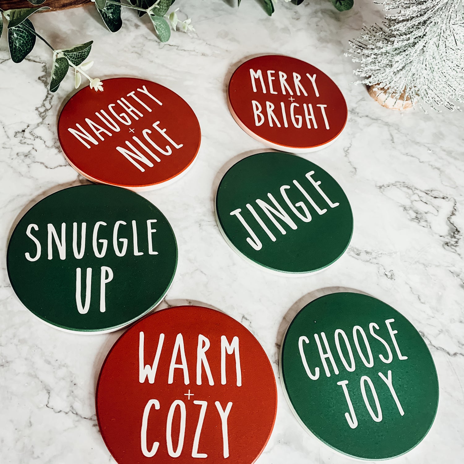 Set of six premium ceramic coasters with cork backing, featuring festive holiday designs including 'Choose Joy' and 'Merry + Bright'.