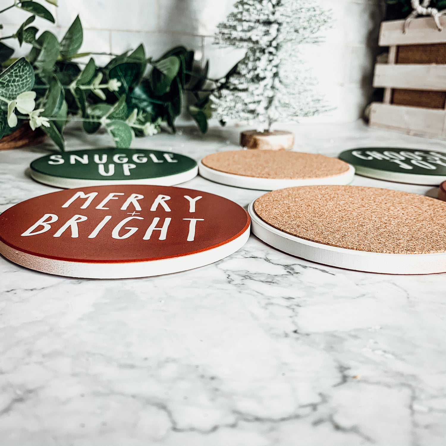 Set of six premium ceramic coasters with cork backing, featuring festive holiday designs including 'Choose Joy' and 'Merry + Bright'.