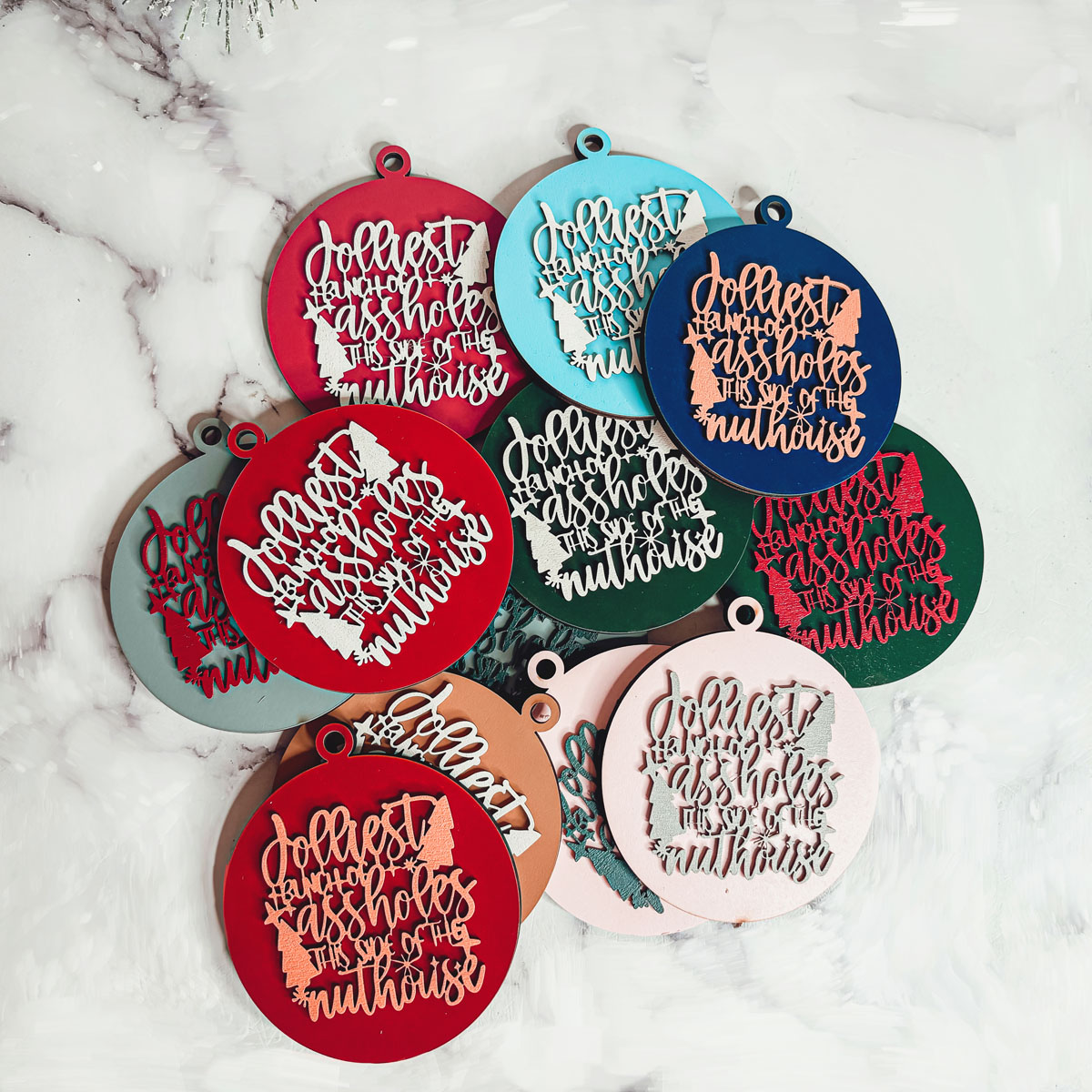 Jolliest Bunch Wooden Ornament featuring festive graphics and rustic twine, available in 12 vibrant colors.