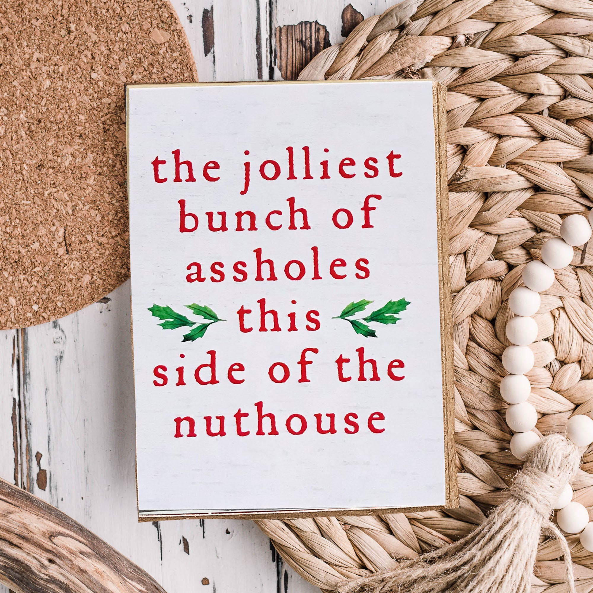 A humorous Christmas sign reading 'The jolliest bunch of assholes this side of the nuthouse', perfect for holiday decor.